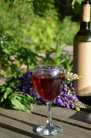 Red wine poured into wine glass on background of green tree leaf foliage. purpie flowerの写真素材