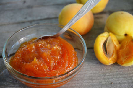 Apricot jam in a glass bowl, fresh apricots in a basket on a light wooden backgroundの写真素材