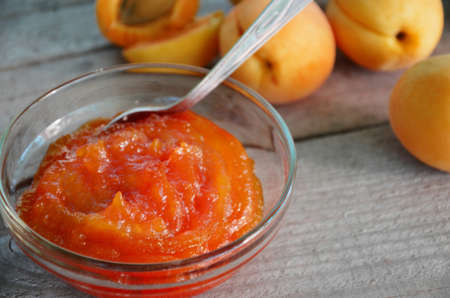 Apricot jam in a glass bowl, fresh apricots in a basket on a light wooden backgroundの写真素材