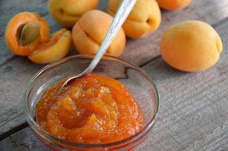 Apricot jam in a glass bowl, fresh apricots in a basket on a light wooden backgroundの写真素材