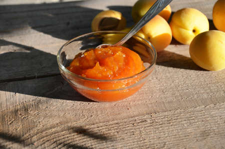 Apricot jam in a glass bowl, fresh apricots in a basket on a light wooden backgroundの写真素材