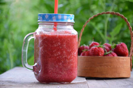 Healthy strawberry smoothie in a mason a jar mug over a rustic wood background against the of green foliage in the gardenの写真素材