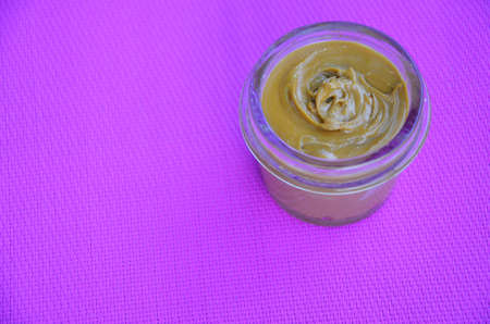 Jar and spoon of peanut butter and peanuts on purple background from top viewの写真素材