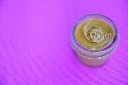 Jar and spoon of peanut butter and peanuts on purple background from top viewの写真素材