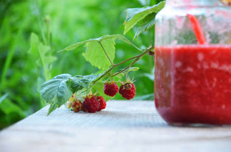 Berry smoothie in a mason jar on a wooden table. against a background of green foliage. in the...