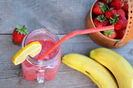 banana and strawberry smoothie in a mason jar on a wooden surface. copy space. top viewの写真素材