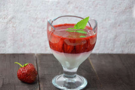 Summer dessert, panna cotta or yogurt or pudding or jam with strawberrieswith strawberries decorated with mint leaves. On a brown wooden table, bright sunlight. Copy space. close upの写真素材
