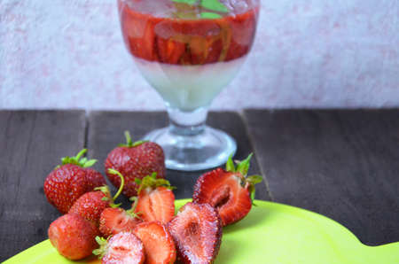 Summer dessert, panna cotta or yogurt or pudding or jam with strawberrieswith strawberries decorated with mint leaves. On a brown wooden table, bright sunlight. Copy space. close upの写真素材