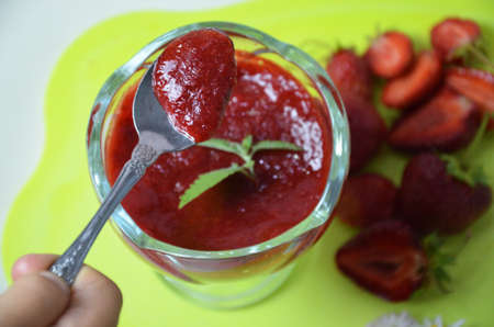 Jars of strawberry jam with berries and spoon on green background tray close upの写真素材