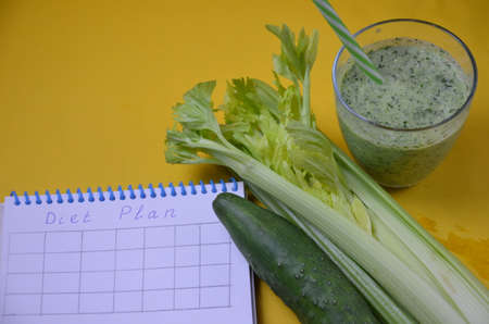 Healthy green smoothie and ingredients on yellow background - superfoods, detox, diet, health, vegetarian food. celery, cucumber, parsley, dill. a diet plan in a notebook.の写真素材