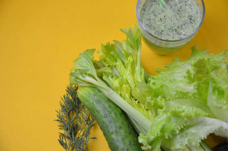 Healthy green smoothie and ingredients on yellow background - superfoods, detox, diet, health, vegetarian food. celery, cucumber, parsley, dill. a diet plan in a notebook.の写真素材