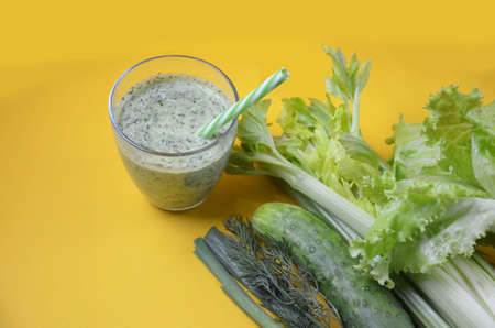 Healthy green smoothie and ingredients on yellow background - superfoods, detox, diet, health, vegetarian food. celery, cucumber, parsley, dill. a diet plan in a notebook.の写真素材