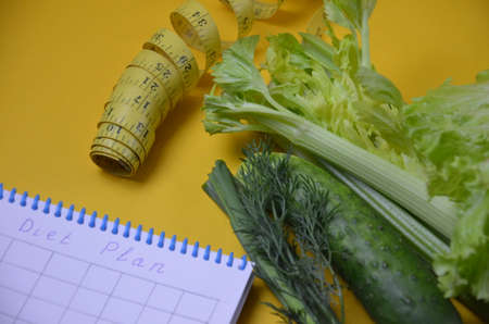 Healthy green smoothie and ingredients on yellow background - superfoods, detox, diet, health, vegetarian food. celery, cucumber, parsley, dill. a diet plan in a notebook.の写真素材