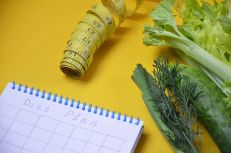 Healthy green smoothie and ingredients on yellow background - superfoods, detox, diet, health, vegetarian food. celery, cucumber, parsley, dill. a diet plan in a notebook.の写真素材