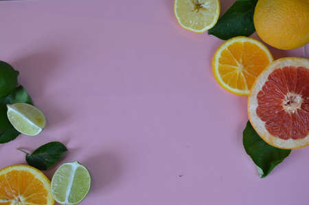Flat lay of citrus fruits like lime and lemon with lemon tree leaves on light pink background making a frame.の写真素材