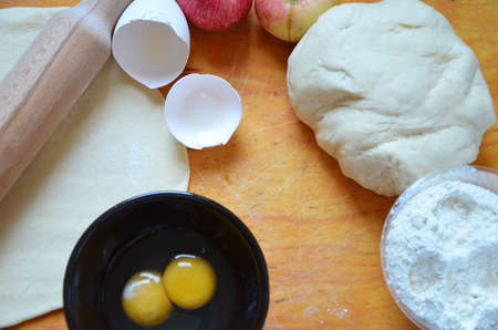 Home autumn, summer baking, puff pastries. Apple strudel with nuts, raisins, cinnamon and powdered sugar. On wooden table. Sliced, with ingredients. Copy space top view. pie ingredientsの写真素材