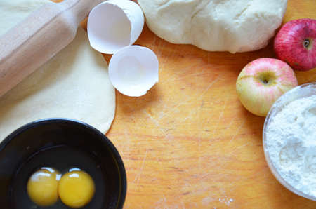 Home autumn, summer baking, puff pastries. Apple strudel with nuts, raisins, cinnamon and powdered sugar. On wooden table. Sliced, with ingredients. Copy space top view. pie ingredientsの写真素材