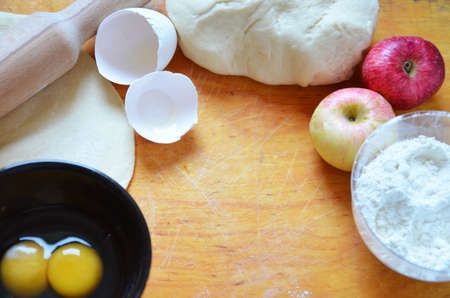 Home autumn, summer baking, puff pastries. Apple strudel with nuts, raisins, cinnamon and powdered sugar. On wooden table. Sliced, with ingredients. Copy space top view. pie ingredientsの写真素材