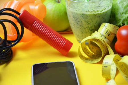 using calorie counter application on her smartphone. fruits and vegetables of different colors, green smoothies. diet vegetarian is a healthy low-calorie food. notebook with a diet planの写真素材