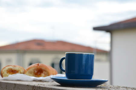 blue cup of coffee with panoramic view of a city in background with croissant. breakfast. on the balcony against the backdrop of the old European city. good morning, romanceの写真素材