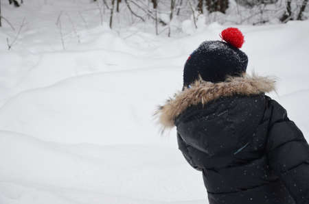 A simpotic little boy throws snow in the winter snow-covered forest, trees in the snow. enjoys the winter. plays snowballs. happy, smiling, laughing with falling snowの写真素材