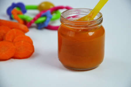 baby carrot mashed, food, puree with spoon in glass jar on white backgroundの写真素材