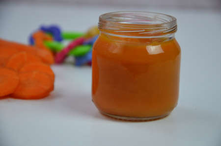 baby carrot mashed, food, puree with spoon in glass jar on white backgroundの写真素材