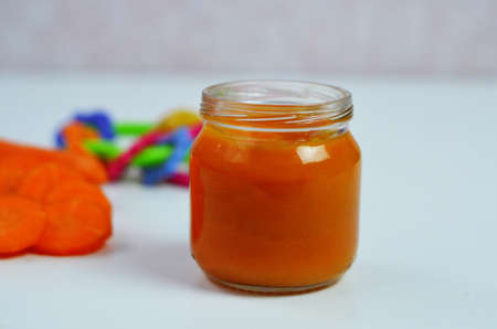 baby carrot mashed, food, puree with spoon in glass jar on white backgroundの写真素材