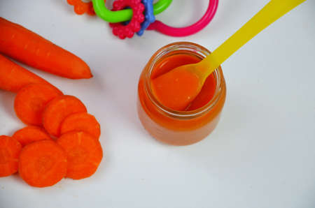 baby carrot mashed, food, puree with spoon in glass jar on white backgroundの写真素材