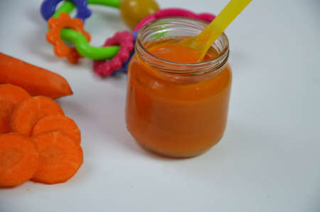baby carrot mashed, food, puree with spoon in glass jar on white backgroundの写真素材