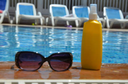 sunglasses and yellow sunscreen near a blue pool outside. concept of vacation, vacation, summer at the side of swimming pool. Vacation, beach, summer travel conceptの写真素材