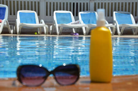 sunglasses and yellow sunscreen near a blue pool outside. concept of vacation, vacation, summer at the side of swimming pool. Vacation, beach, summer travel conceptの写真素材