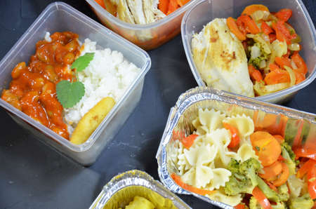 Healthy food and diet concept, restaurant dish delivery. Take away of fitness meal. Weight loss nutrition in foil boxes. eats and works computer. Food storage in containers. Freelance. Work at homeの写真素材