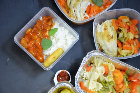 Healthy food and diet concept, restaurant dish delivery. Take away of fitness meal. Weight loss nutrition in foil boxes. eats and works computer. Food storage in containers. Freelance. Work at homeの写真素材