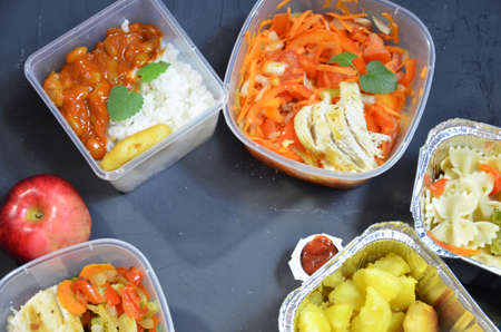 Healthy food and diet concept, restaurant dish delivery. Take away of fitness meal. Weight loss nutrition in foil boxes. eats and works computer. Food storage in containers. Freelance. Work at homeの写真素材