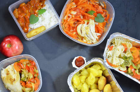 Healthy food and diet concept, restaurant dish delivery. Take away of fitness meal. Weight loss nutrition in foil boxes. eats and works computer. Food storage in containers. Freelance. Work at homeの写真素材