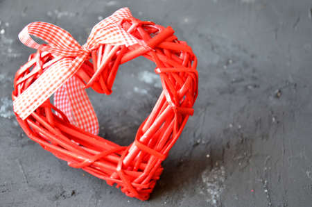 a red heart made of wood texture. A celebration of love. Valentine's day. wicker red heart with bow and ribbon on black background.の写真素材