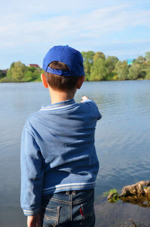 A boy stands by the forest lake and looks at the calm water. Nature, contemplation, inspiration,...