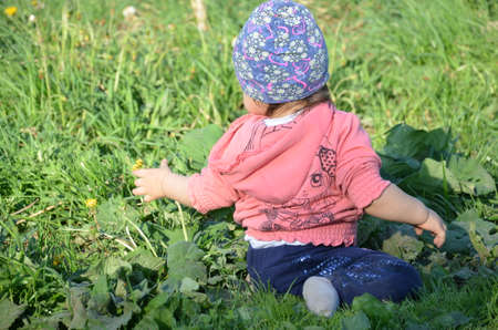 Smiling cute playful little girl is standing on green grass. girl toddler walks around the lake learns to walk. spring or summerの写真素材