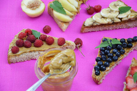 Composition different delicious toasts on green or pink crimson background. Healthy sandwich for breakfast or snack. Toast with raspberries, strawberries, banana and blueberries and peanut butter. picnicの写真素材