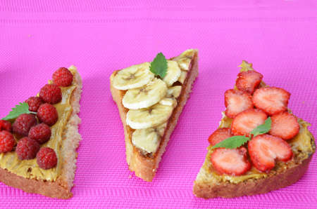 Composition different delicious toasts on green or pink crimson background. Healthy sandwich for breakfast or snack. Toast with raspberries, strawberries, banana and blueberries and peanut butter. picnicの写真素材