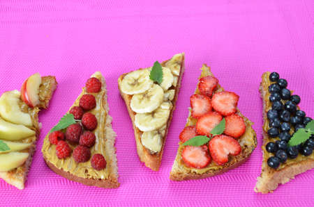 Composition different delicious toasts on green or pink crimson background. Healthy sandwich for breakfast or snack. Toast with raspberries, strawberries, banana and blueberries and peanut butter. picnicの写真素材