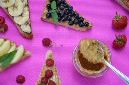 Composition different delicious toasts on green or pink crimson background. Healthy sandwich for breakfast or snack. Toast with raspberries, strawberries, banana and blueberries and peanut butter. picnicの写真素材