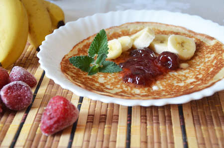 freshly fried homemade french crepes on a plate with strawberries, banana slices and fresh cream, horizontal view from above, close-upの写真素材