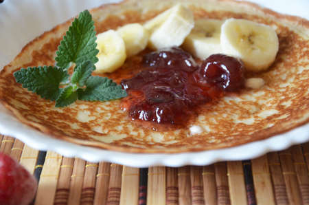 freshly fried homemade french crepes on a plate with strawberries, banana slices and fresh cream, horizontal view from above, close-upの写真素材