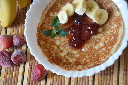freshly fried homemade french crepes on a plate with strawberries, banana slices and fresh cream, horizontal view from above, close-upの写真素材