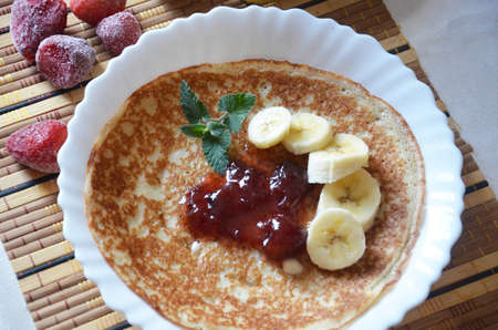 freshly fried homemade french crepes on a plate with strawberries, banana slices and fresh cream, horizontal view from above, close-upの写真素材