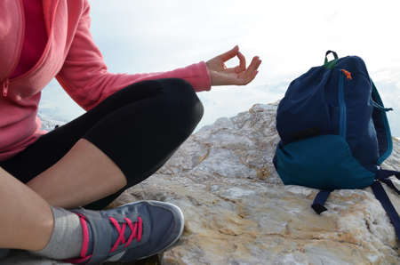 young woman meditation in a yoga pose at the beach. girl in lotus position on an empty stone seashore. takes yoga, sports, meditation. healthy lifestyle. close up sneakers sportswear.の写真素材