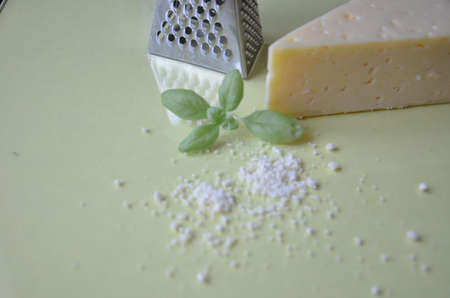 grated parmesan cheese and metal grater on grated parmesan cheese and metal grater on yellow background. Ingredients for cooking traditional Italian dishes. Spaghetti, pasta, pizza. Italian hard parmesan cheese, fresh green basil.の写真素材