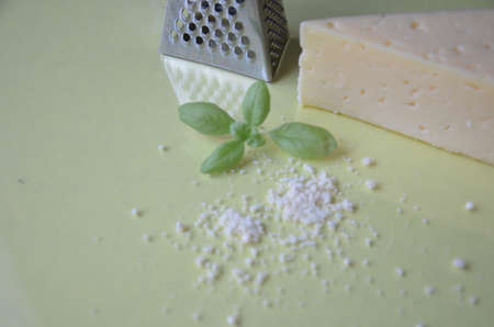 grated parmesan cheese and metal grater on grated parmesan cheese and metal grater on yellow background. Ingredients for cooking traditional Italian dishes. Spaghetti, pasta, pizza. Italian hard parmesan cheese, fresh green basil.の写真素材